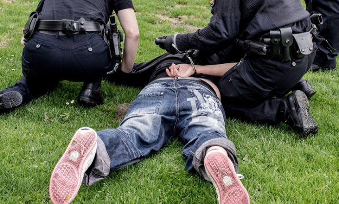 Zwei Polizisten legen einem am Boden liegenden Mann Handschellen an